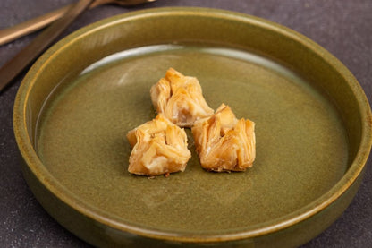 Three Bukaj cashew baklava on a green plate with a decorative background